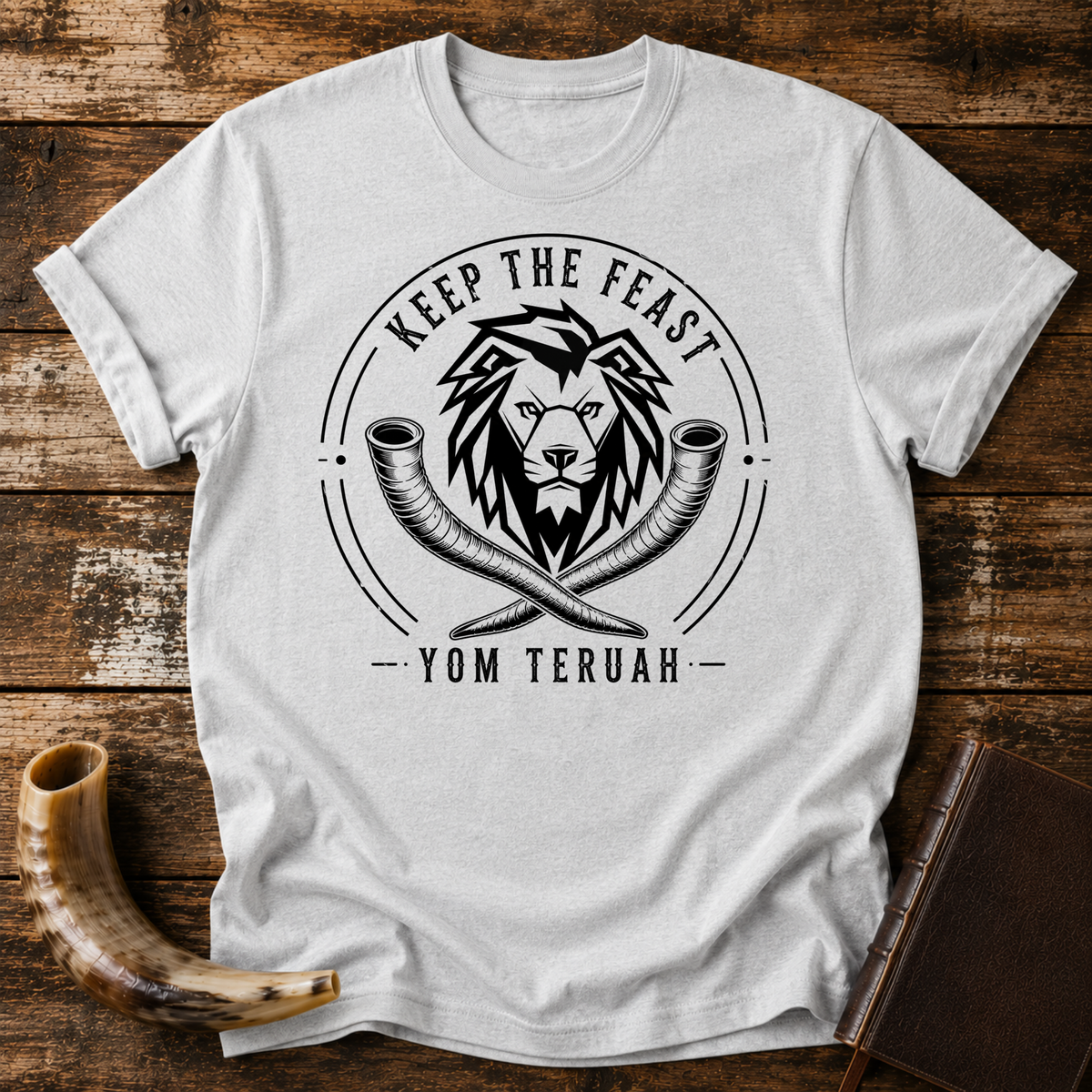 Sport grey t-shirt with a black lion head over crossed shofars, KEEP THE FEAST YOM TERUAH, laid flat with a shofar and a leather book