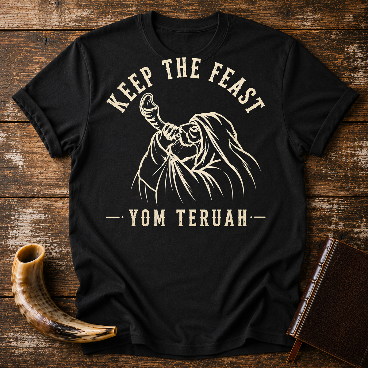Black t-shirt with KEEP THE FEAST YOM TERUAH and a robed man blowing a shofar, laid flat with a shofar and a leather book
