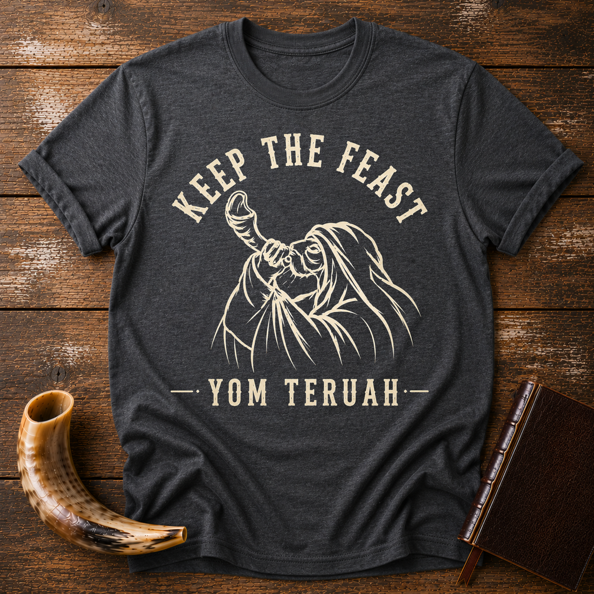 Dark heather gray t-shirt with KEEP THE FEAST YOM TERUAH and a robed man blowing a shofar, laid flat with a shofar and a leather book