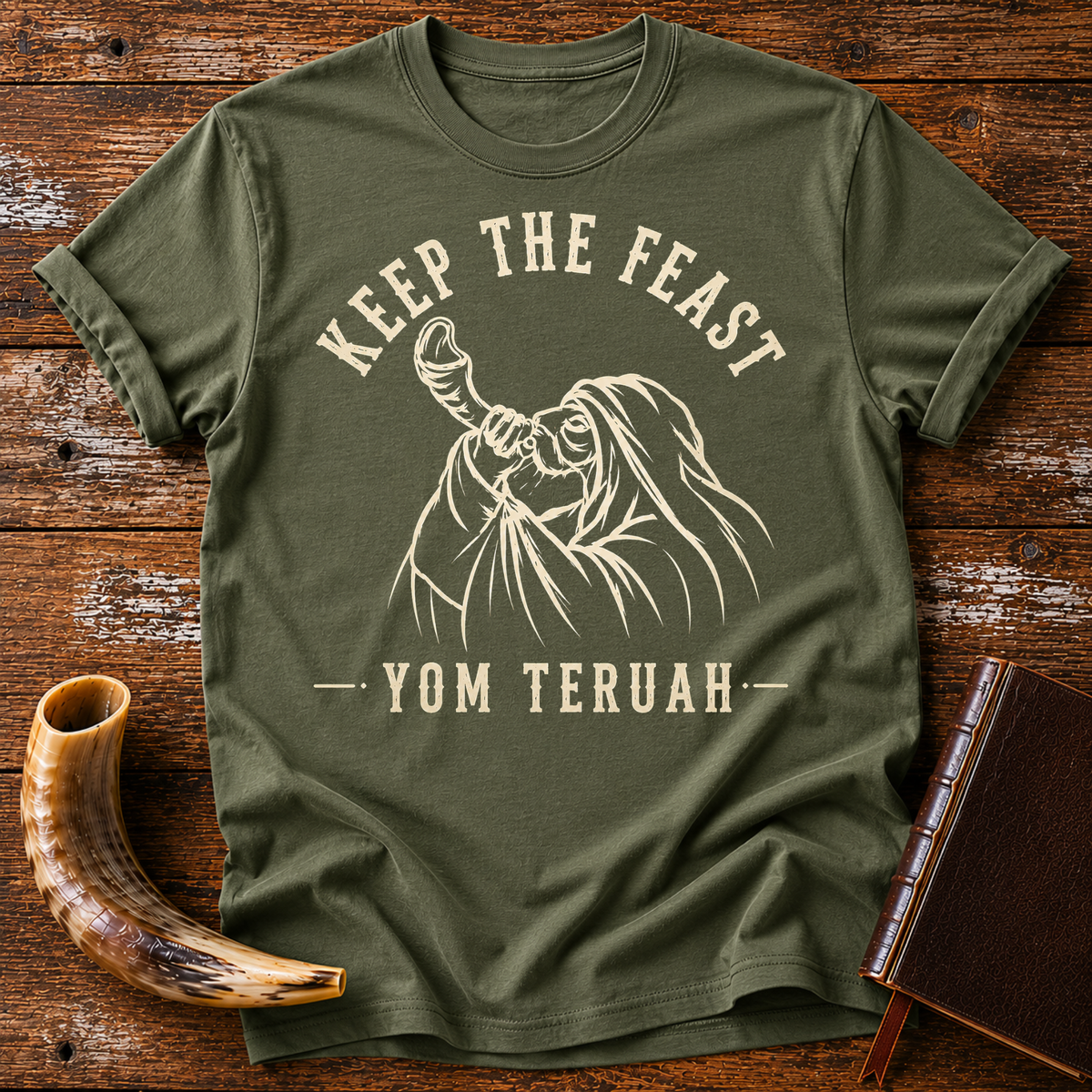 Military green t-shirt with KEEP THE FEAST YOM TERUAH and a robed man blowing a shofar, laid flat with a shofar and a leather book