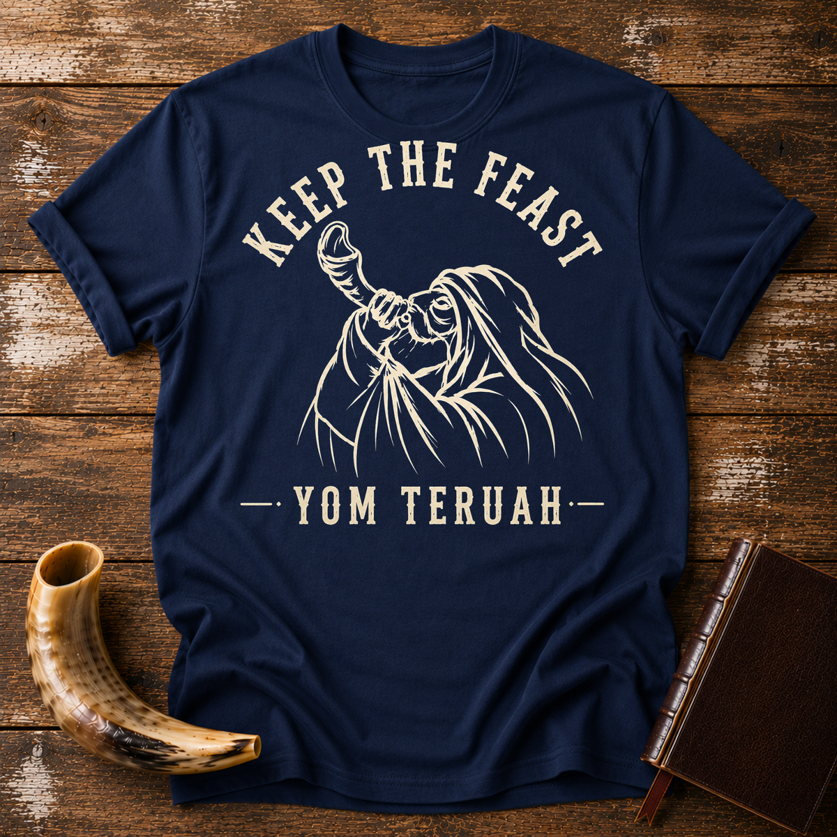 Navy t-shirt with KEEP THE FEAST YOM TERUAH and a robed man blowing a shofar, laid flat with a shofar and a leather book