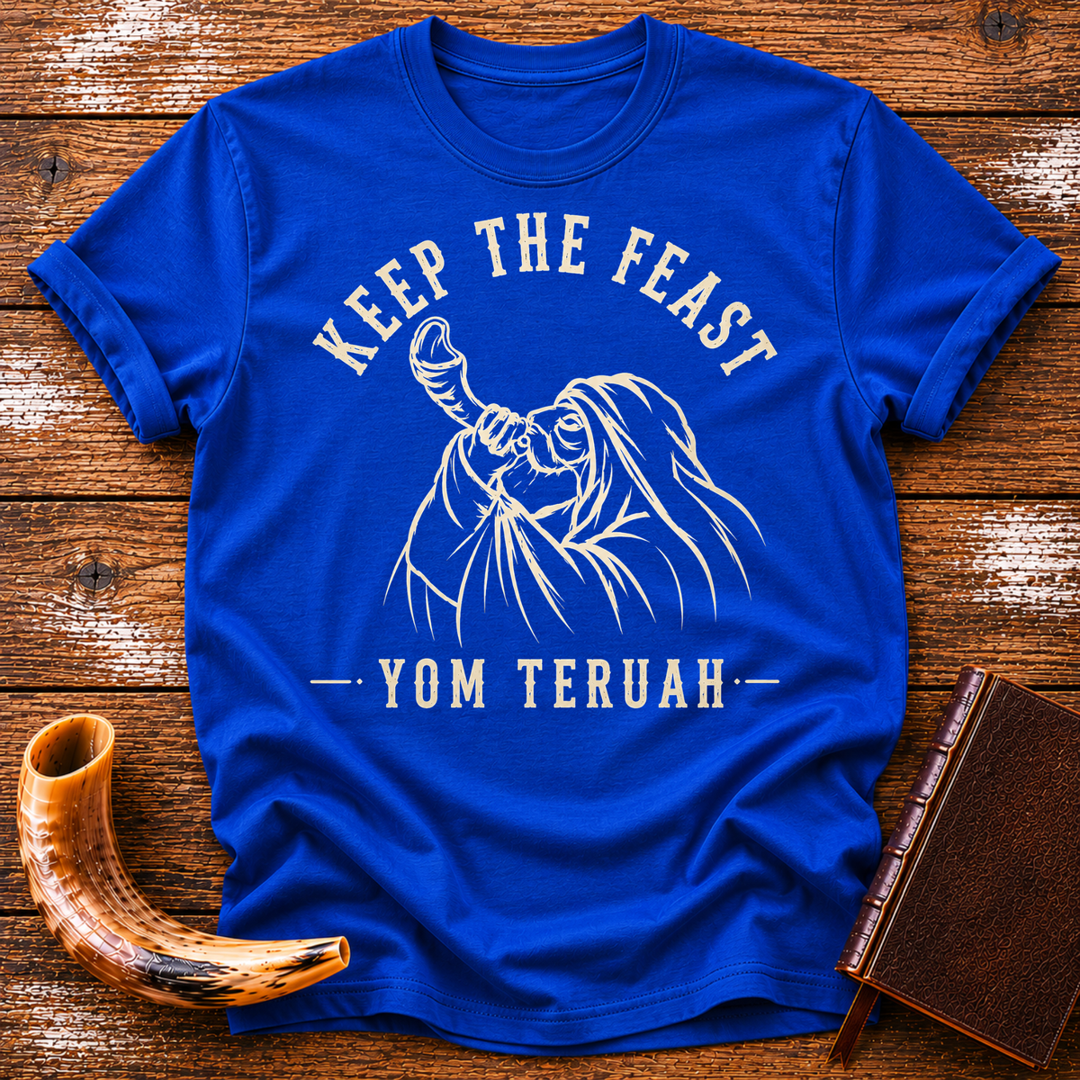Royal blue t-shirt with KEEP THE FEAST YOM TERUAH and a robed man blowing a shofar, laid flat with a shofar and a leather book
